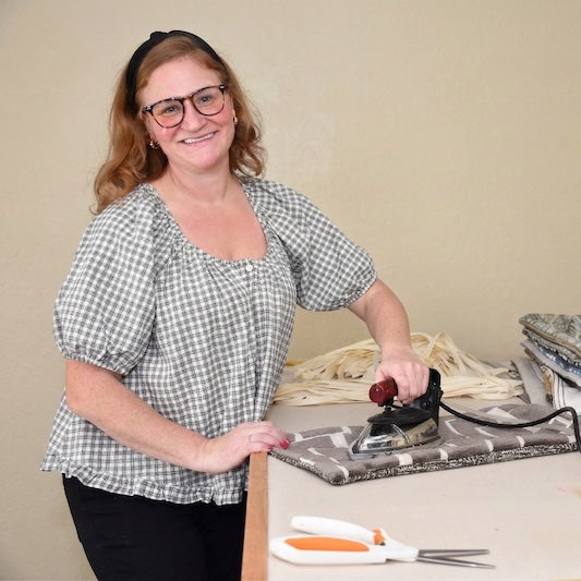 Woman ironing fabric on an ironing board with various materials and tools around.